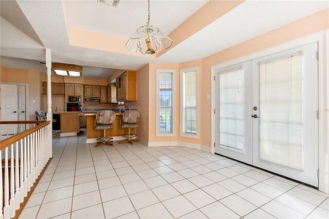 kitchen featuring french doors, stainless steel microwave, pendant lighting, a notable chandelier, and a tray ceiling