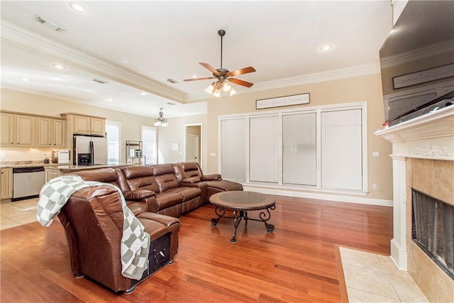 living room with ceiling fan with notable chandelier, ornamental molding, a fireplace, and light hardwood / wood-style floors