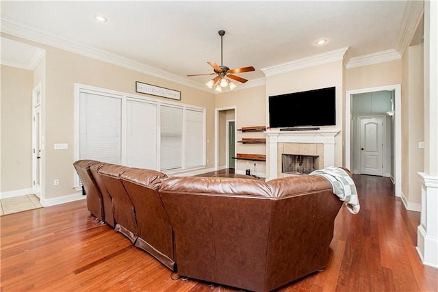 living room featuring ceiling fan, hardwood / wood-style flooring, a tiled fireplace, and crown molding