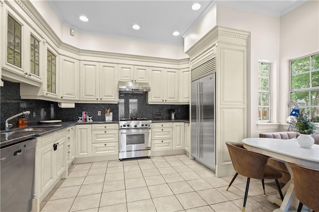 kitchen featuring high quality appliances, sink, crown molding, light tile patterned floors, and backsplash