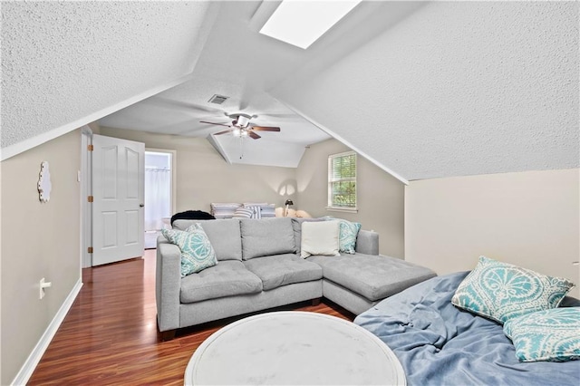 living room with a textured ceiling, ceiling fan, vaulted ceiling with skylight, and dark hardwood / wood-style flooring