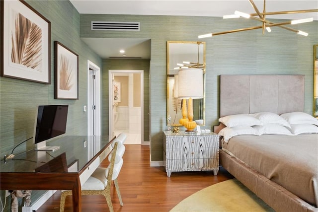 bedroom with ensuite bath, wood-type flooring, and an inviting chandelier