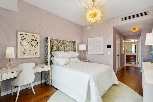 bedroom with ensuite bath, dark wood-type flooring, and an inviting chandelier