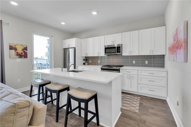 kitchen with appliances with stainless steel finishes, white cabinetry, wood-type flooring, and an island with sink