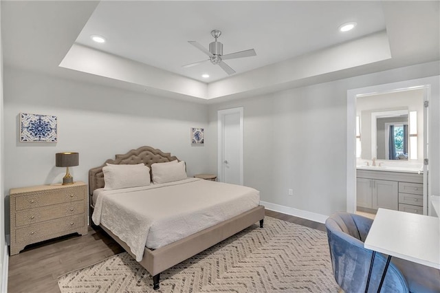 bedroom featuring ceiling fan, sink, light hardwood / wood-style flooring, a tray ceiling, and ensuite bath