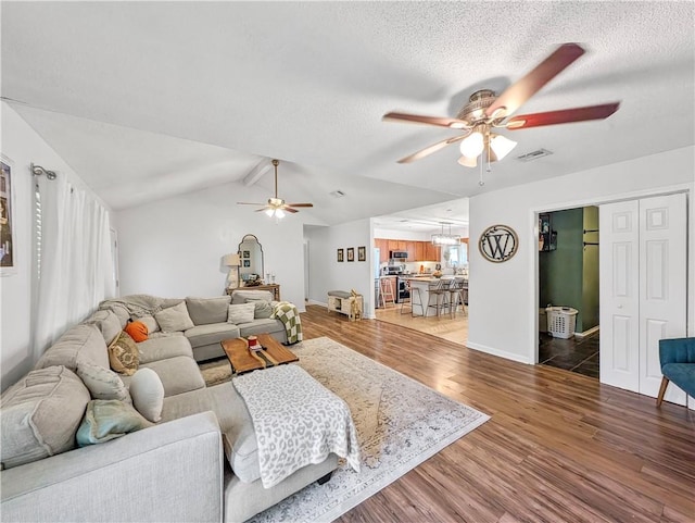 living room featuring ceiling fan, hardwood / wood-style floors, lofted ceiling with beams, and a textured ceiling