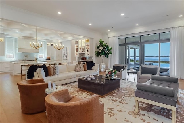 living room with a notable chandelier, crown molding, light hardwood / wood-style floors, and a water view