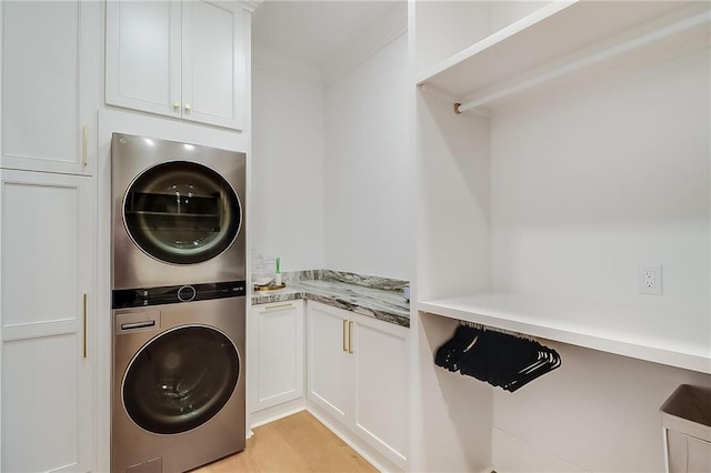 clothes washing area with ornamental molding, light wood-type flooring, stacked washer / dryer, and cabinets