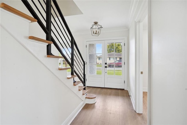 entrance foyer with french doors, a notable chandelier, crown molding, and light hardwood / wood-style floors