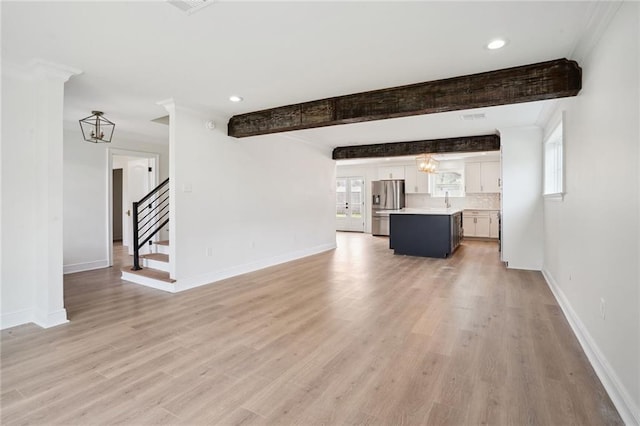 unfurnished living room with light hardwood / wood-style floors, beamed ceiling, and a notable chandelier