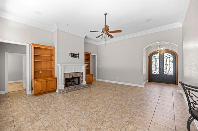 tiled entryway with french doors, ceiling fan with notable chandelier, a brick fireplace, and ornamental molding