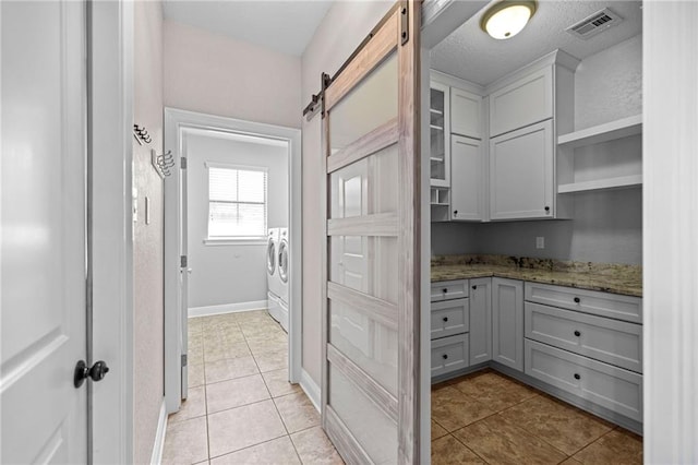 kitchen with light stone counters, a barn door, washing machine and dryer, gray cabinets, and light tile patterned floors