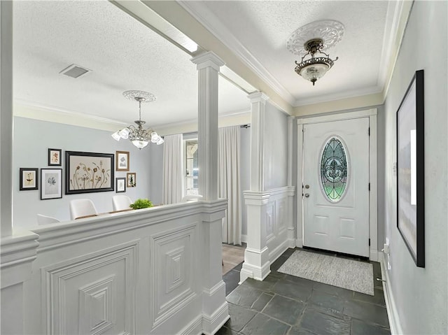 entrance foyer featuring an inviting chandelier, a textured ceiling, crown molding, and ornate columns