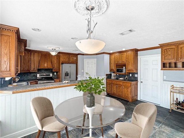 kitchen featuring decorative light fixtures, sink, tile counters, kitchen peninsula, and appliances with stainless steel finishes