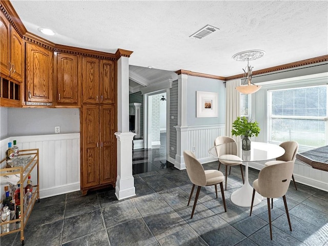 dining space with ornate columns, crown molding, and a textured ceiling