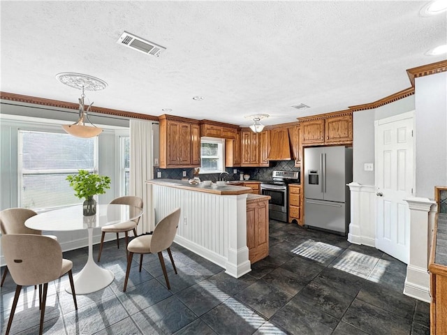 kitchen with pendant lighting, kitchen peninsula, backsplash, appliances with stainless steel finishes, and ornamental molding