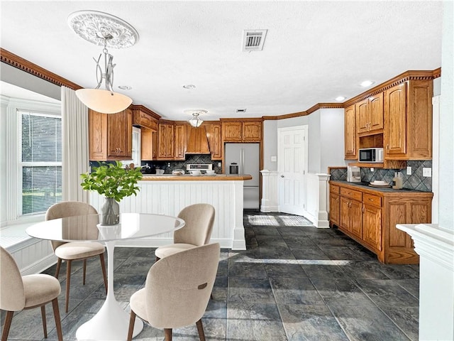 kitchen featuring backsplash, custom range hood, stainless steel appliances, hanging light fixtures, and ornamental molding