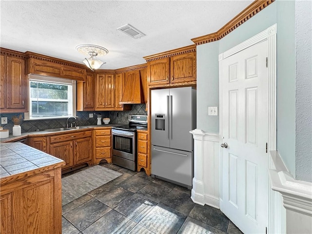 kitchen with decorative backsplash, stainless steel appliances, sink, tile counters, and a textured ceiling