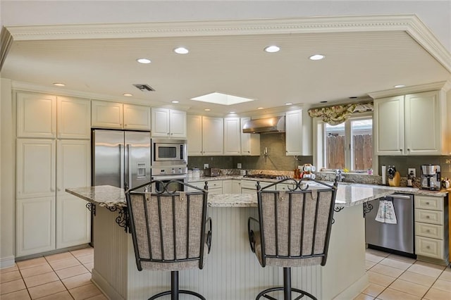 kitchen with a kitchen island, light stone countertops, wall chimney range hood, and stainless steel appliances