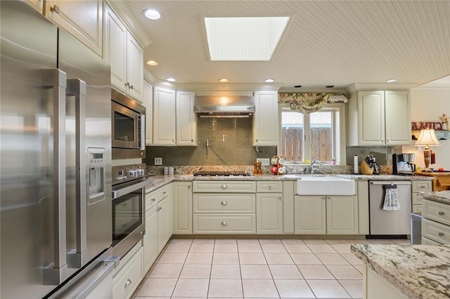 kitchen featuring light stone countertops, stainless steel appliances, wall chimney exhaust hood, sink, and a skylight