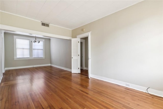 empty room featuring wood-type flooring, a notable chandelier, and ornamental molding