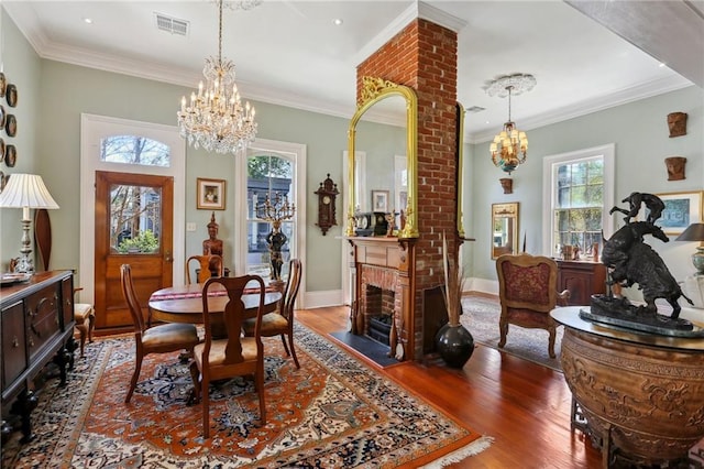 dining area with a brick fireplace, dark wood-type flooring, ornate columns, an inviting chandelier, and ornamental molding