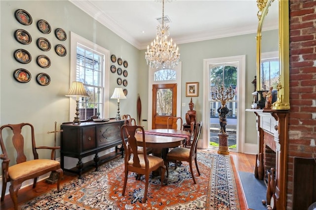 dining room featuring light wood-type flooring, crown molding, a fireplace, and a chandelier