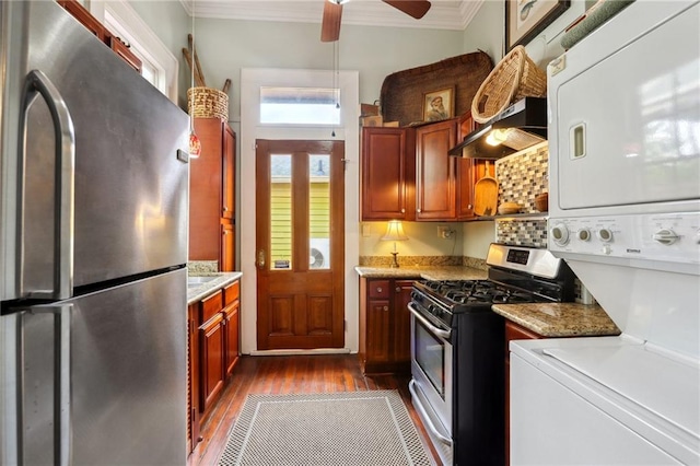 kitchen with light stone counters, dark wood-type flooring, stainless steel appliances, crown molding, and stacked washer and dryer