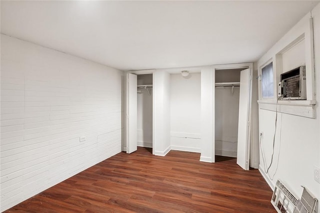 unfurnished bedroom featuring two closets, brick wall, and dark hardwood / wood-style flooring