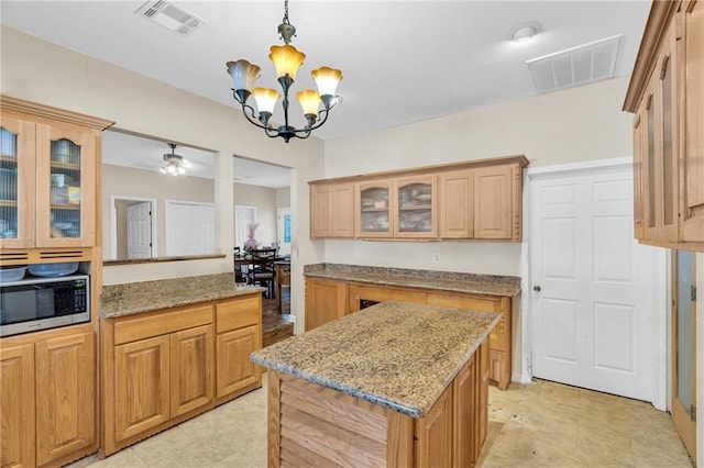 kitchen featuring ceiling fan with notable chandelier, light stone countertops, decorative light fixtures, and a kitchen island