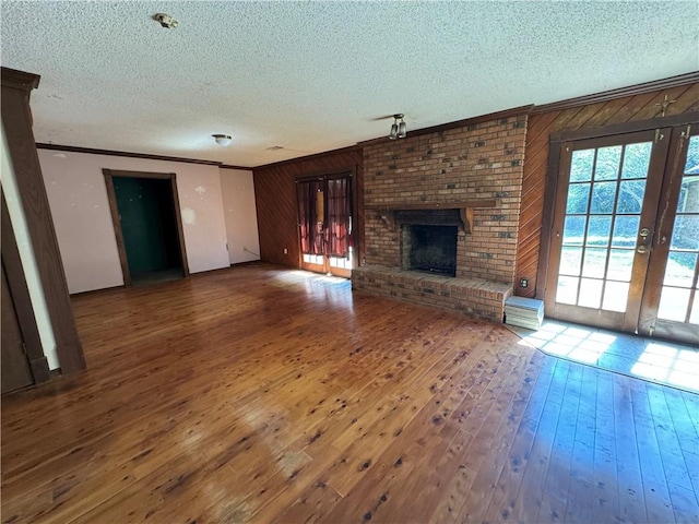 unfurnished living room featuring ornamental molding, wood-type flooring, a brick fireplace, a textured ceiling, and wooden walls