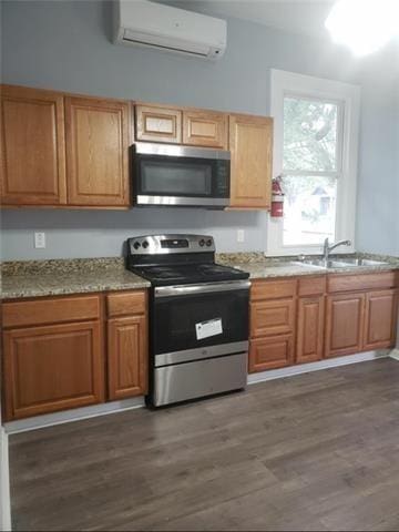 kitchen featuring light stone counters, a wall mounted air conditioner, stainless steel appliances, dark wood-type flooring, and sink