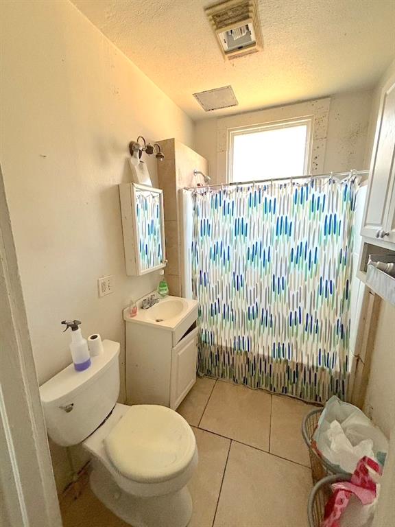 full bathroom with tile patterned flooring, shower / bath combination with curtain, a textured ceiling, vanity, and toilet