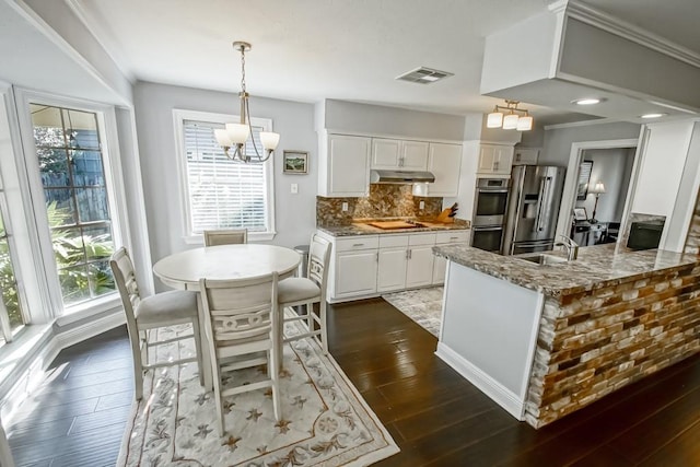 kitchen with white cabinets, kitchen peninsula, appliances with stainless steel finishes, dark hardwood / wood-style floors, and light stone countertops