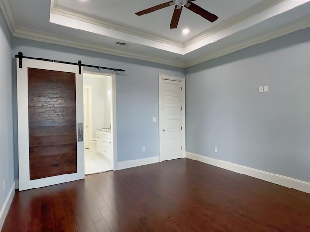 unfurnished bedroom featuring dark wood-type flooring, a barn door, ensuite bathroom, a raised ceiling, and crown molding