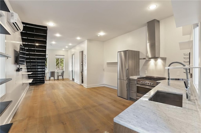 kitchen with stainless steel appliances, light hardwood / wood-style flooring, wall chimney exhaust hood, and light stone counters