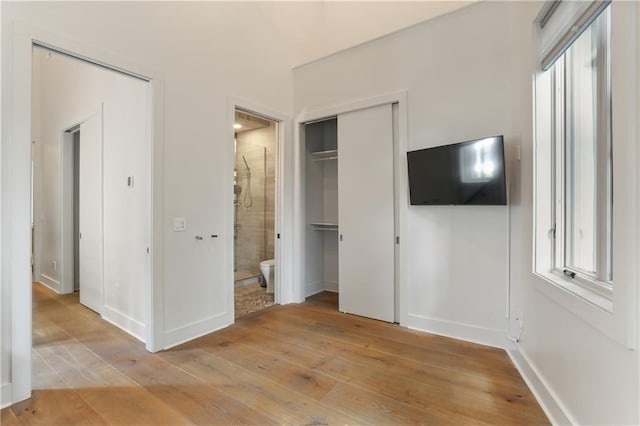 unfurnished bedroom with a closet, ensuite bath, and light hardwood / wood-style floors