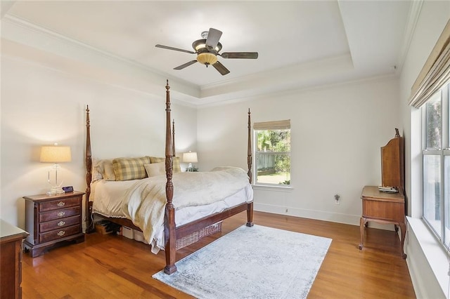 bedroom with baseboards, wood finished floors, a raised ceiling, and ornamental molding