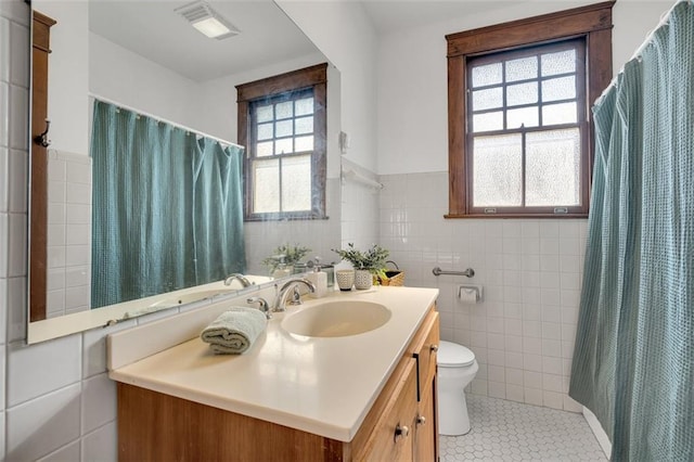 bathroom with plenty of natural light, tile walls, vanity, and toilet