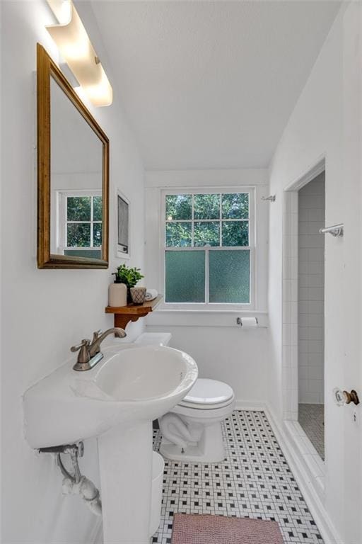 bathroom featuring lofted ceiling, tile patterned flooring, toilet, and tiled shower