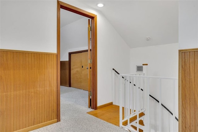 hallway featuring wood walls, vaulted ceiling, and light carpet