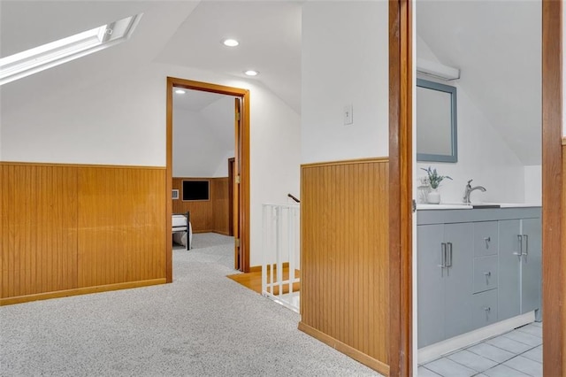 corridor featuring light carpet, wood walls, and lofted ceiling with skylight