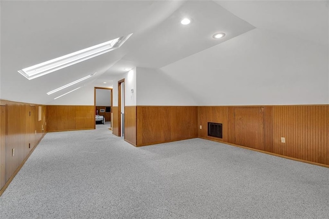 additional living space with wood walls, light carpet, and lofted ceiling with skylight