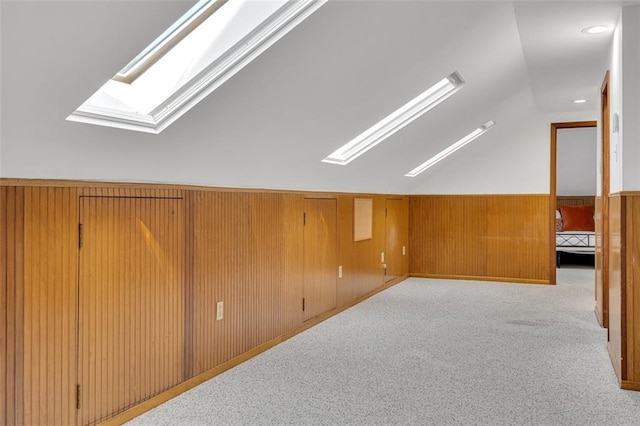 bonus room with light carpet, wood walls, and vaulted ceiling with skylight