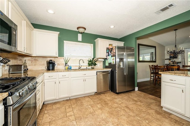 kitchen featuring a notable chandelier, sink, stainless steel appliances, light stone countertops, and white cabinetry