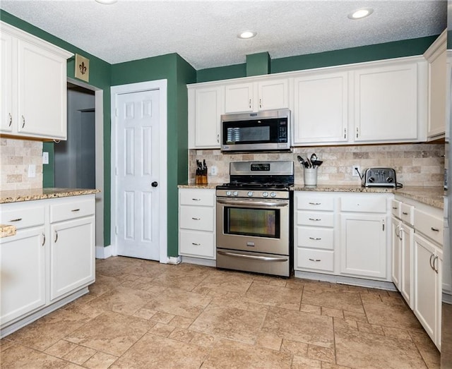 kitchen with light stone counters, decorative backsplash, stainless steel appliances, white cabinetry, and a textured ceiling