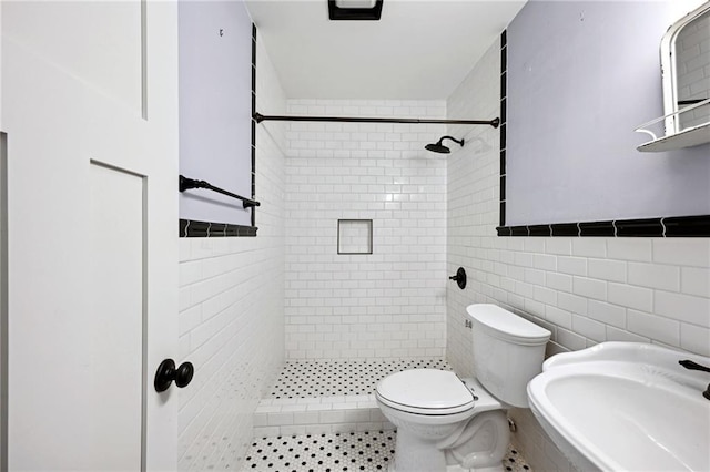 bathroom featuring a tile shower, sink, tile walls, and toilet