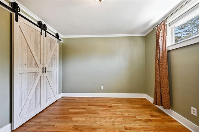 unfurnished bedroom featuring ornamental molding, light wood-type flooring, and a barn door