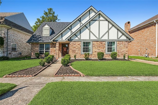 tudor house featuring stucco siding, a shingled roof, a front lawn, and brick siding