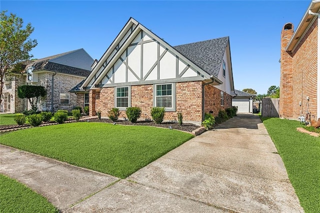 english style home featuring brick siding, roof with shingles, a front lawn, and stucco siding